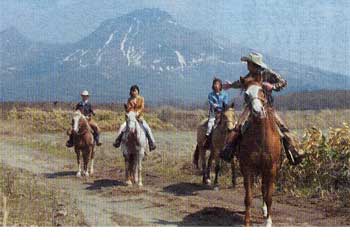 駒ケ岳をバックに乗馬体験をしている青いぽすと記者